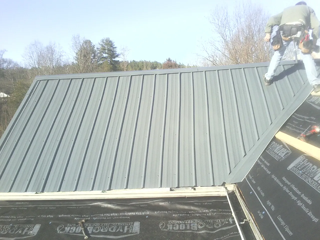 Crew installing dark green standing seam panels over synthetic underlayment in Lincolnton
