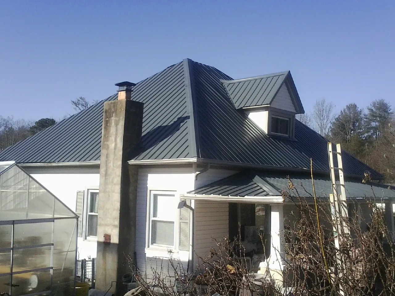 Dark blue standing seam metal roof on a white farmhouse with dormer — Slate & Tile Roof Repair by Roofing Brothers in Lincolnton