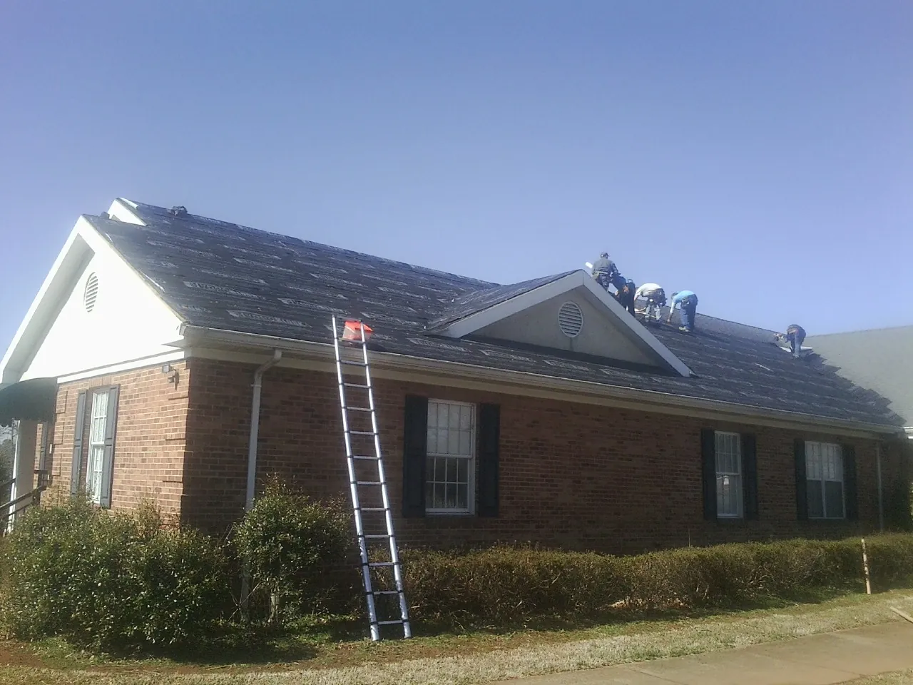 Crew tearing shingles off a brick ranch roof with a ladder set — Metal Roof Repair work by our crew in Lincolnton