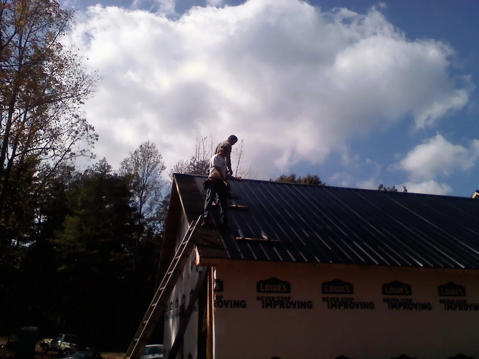 Roofer fastening dark metal panels high against a cloudy sky, from a Roof Inspection job in Lincolnton