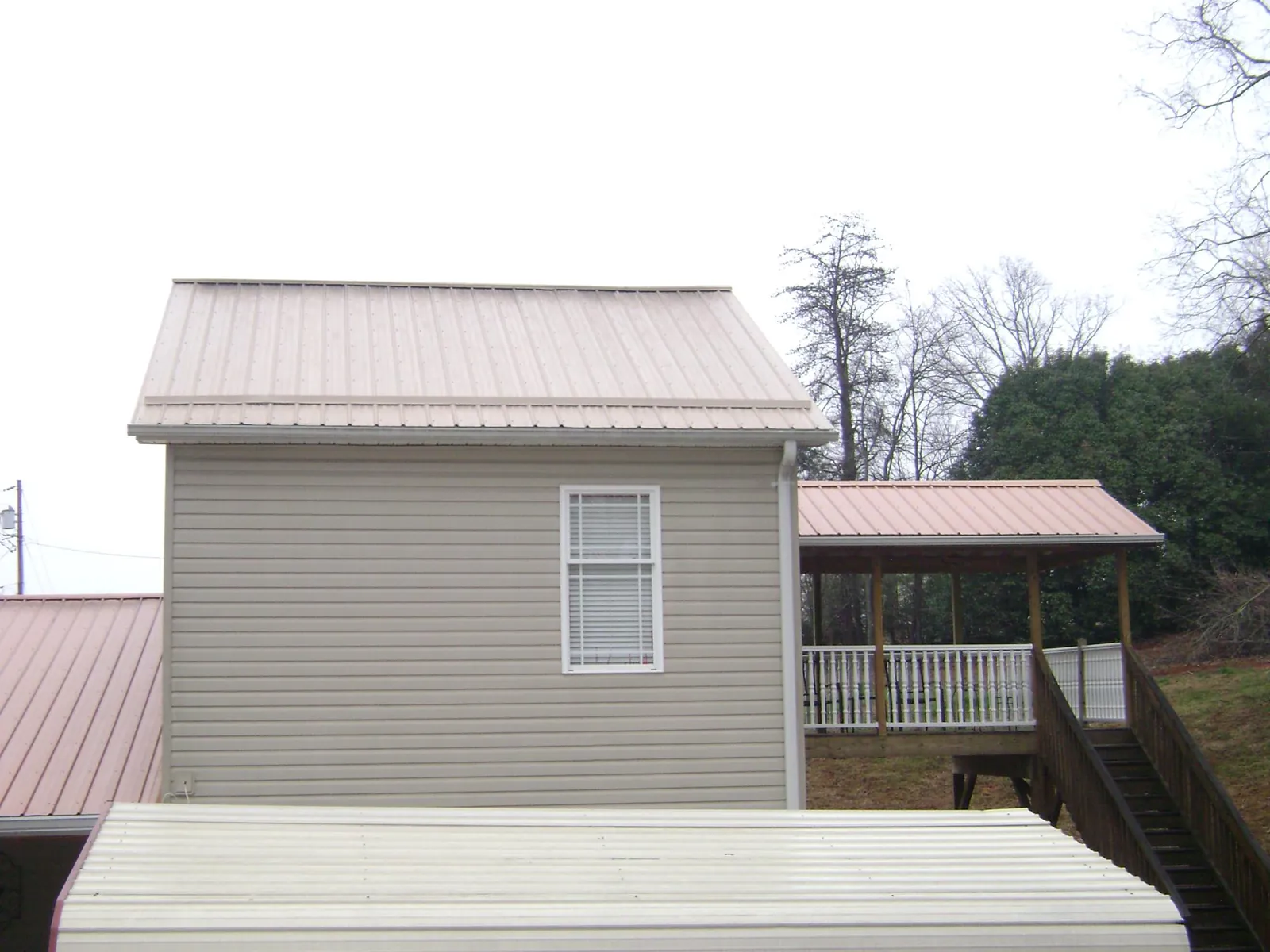 Tan metal roofs on a two story addition and attached porch, from a Roof Replacement job in Lincolnton
